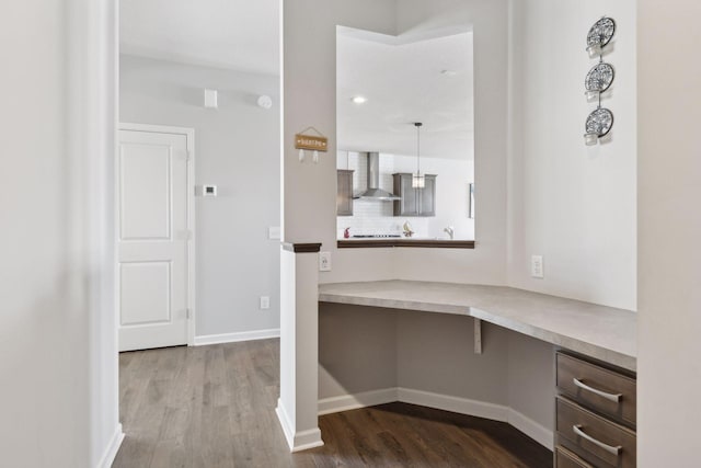 unfurnished office featuring baseboards, built in desk, and wood finished floors