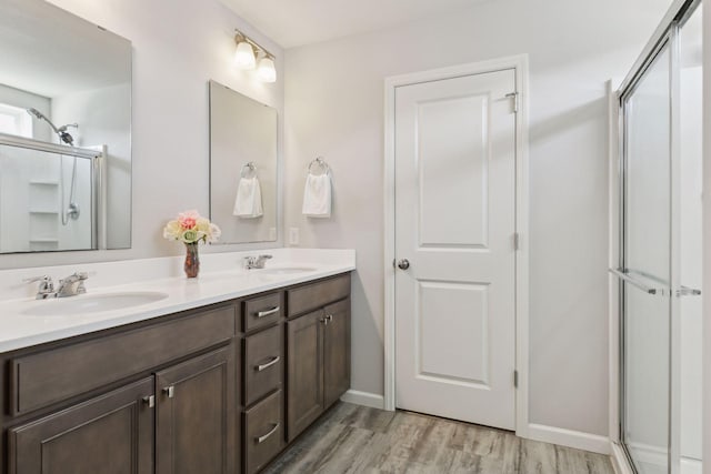 full bath featuring double vanity, a shower stall, a sink, and wood finished floors