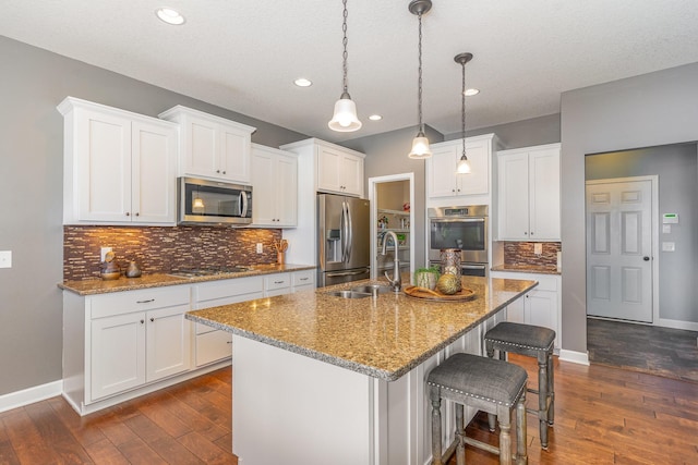 kitchen featuring white cabinetry, a center island with sink, appliances with stainless steel finishes, a breakfast bar area, and pendant lighting