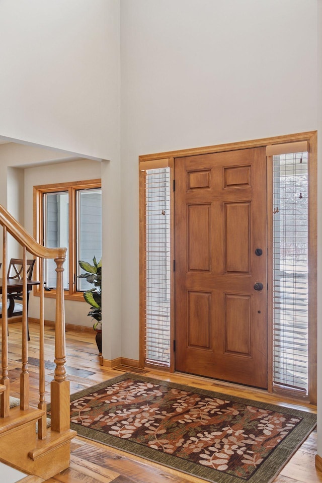 foyer with stairs, a high ceiling, light wood-style floors, and baseboards