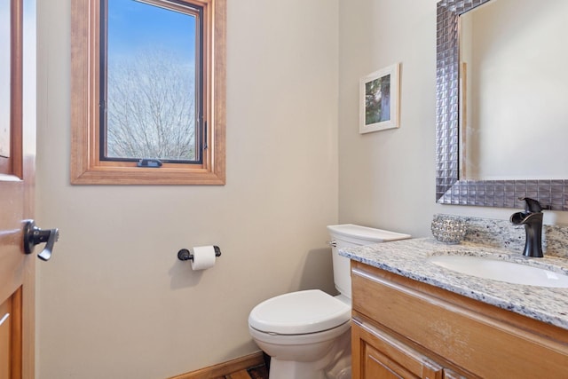 half bathroom featuring vanity, toilet, and baseboards