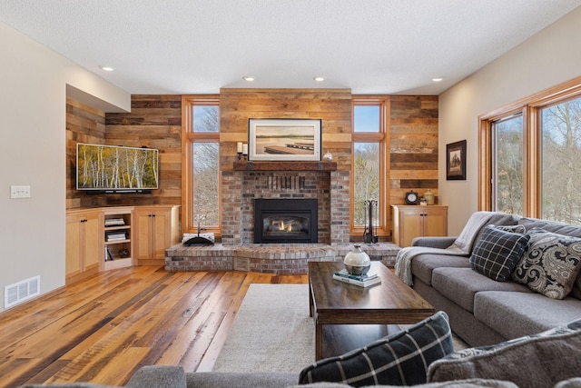 living area with light wood finished floors, visible vents, a fireplace, and wooden walls