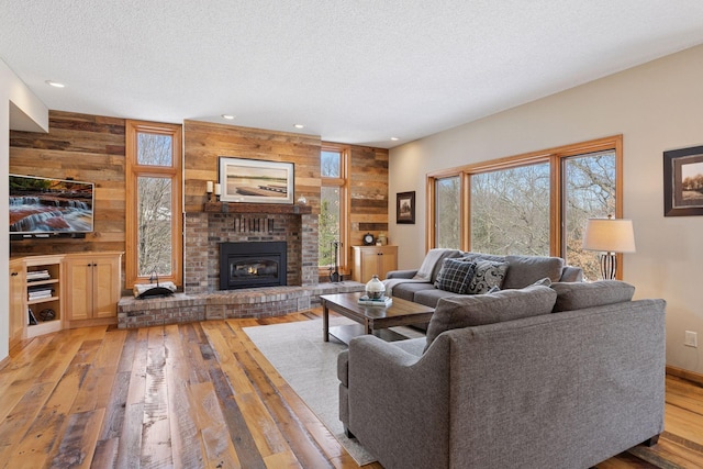 living area with light wood finished floors, a fireplace, wood walls, and a textured ceiling