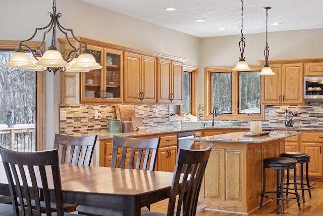 kitchen featuring light stone counters, a sink, glass insert cabinets, light wood-style floors, and a center island