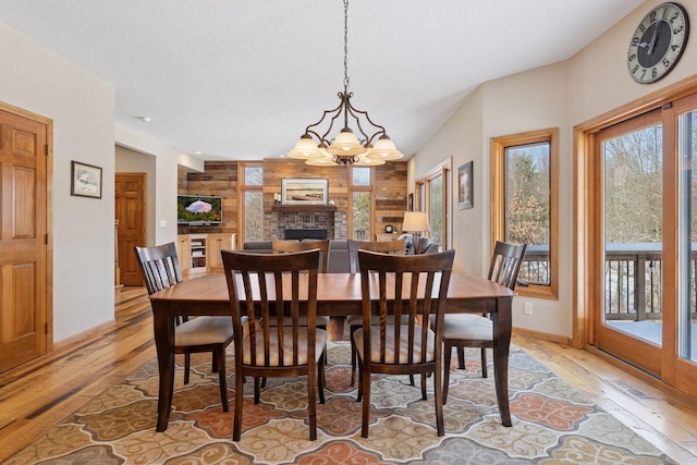 dining space with a notable chandelier, light wood-style flooring, a fireplace, and wooden walls