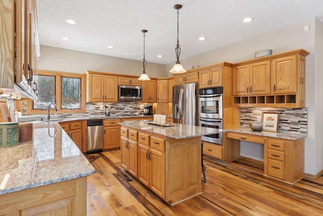 kitchen featuring a sink, a center island, light wood-style floors, appliances with stainless steel finishes, and light stone countertops