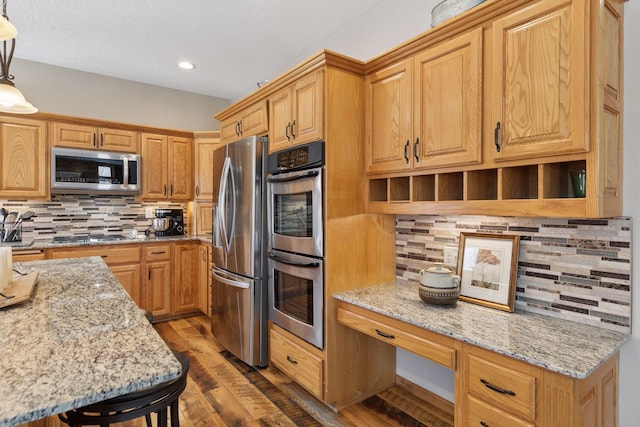 kitchen with light stone counters, tasteful backsplash, appliances with stainless steel finishes, dark wood-style flooring, and built in study area