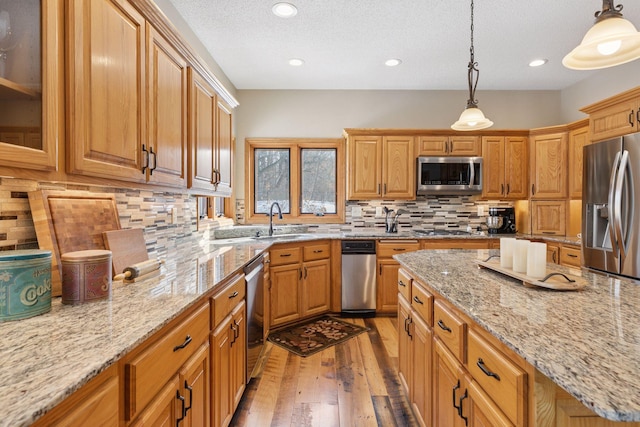 kitchen with light stone countertops, decorative backsplash, appliances with stainless steel finishes, light wood-style floors, and a sink