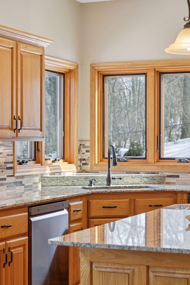 kitchen with stainless steel dishwasher, light stone countertops, backsplash, and a sink