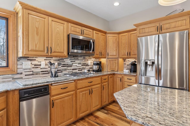 kitchen featuring light stone counters, decorative backsplash, appliances with stainless steel finishes, and light wood-style floors