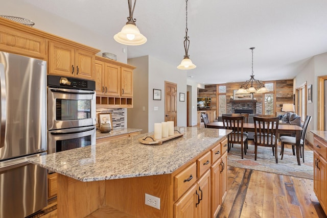 kitchen with backsplash, a kitchen island, a large fireplace, light wood-style floors, and stainless steel appliances