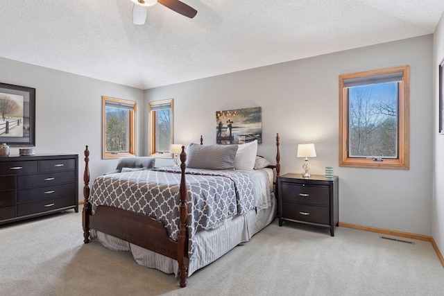 bedroom featuring baseboards, light carpet, a textured ceiling, and ceiling fan