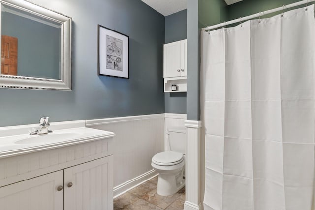 bathroom with a shower with shower curtain, vanity, toilet, and wainscoting