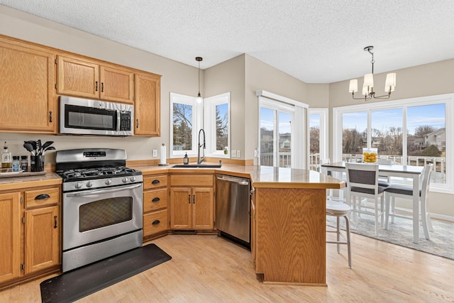 kitchen featuring appliances with stainless steel finishes, hanging light fixtures, a peninsula, light countertops, and a sink