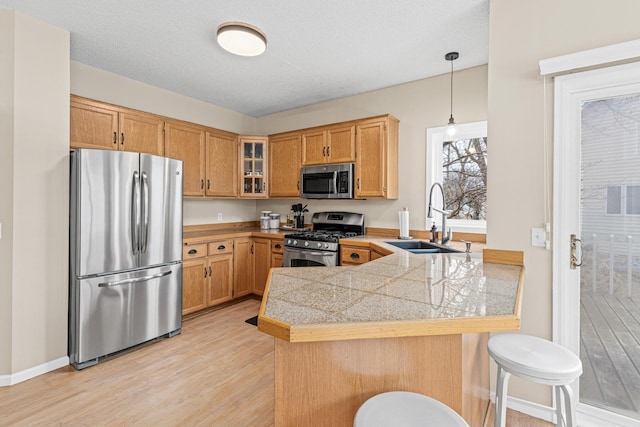 kitchen with tile countertops, appliances with stainless steel finishes, glass insert cabinets, a peninsula, and a sink