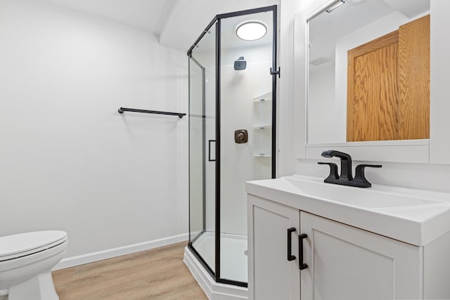 bathroom featuring toilet, wood finished floors, vanity, baseboards, and a stall shower