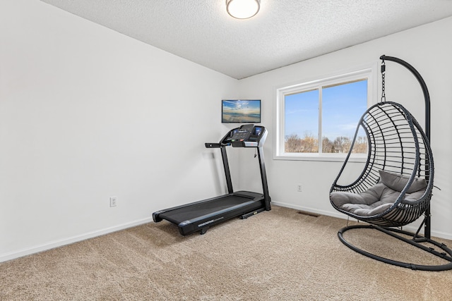 workout area featuring carpet floors, a textured ceiling, and baseboards