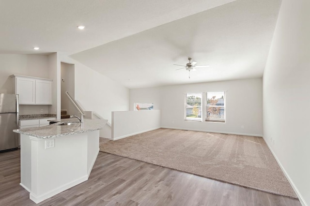 kitchen with vaulted ceiling, light stone counters, freestanding refrigerator, white cabinetry, and a sink