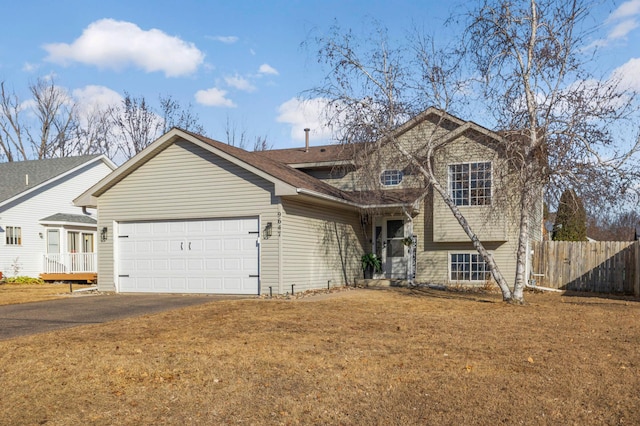 tri-level home featuring aphalt driveway, a front lawn, an attached garage, and fence