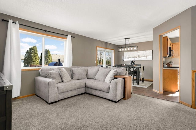 carpeted living area with plenty of natural light, a textured ceiling, baseboards, and an inviting chandelier