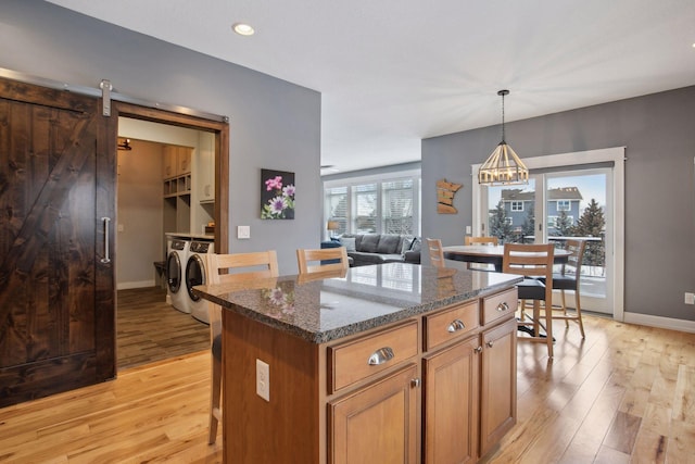 kitchen featuring washer and dryer, pendant lighting, a kitchen island, dark stone counters, and a barn door