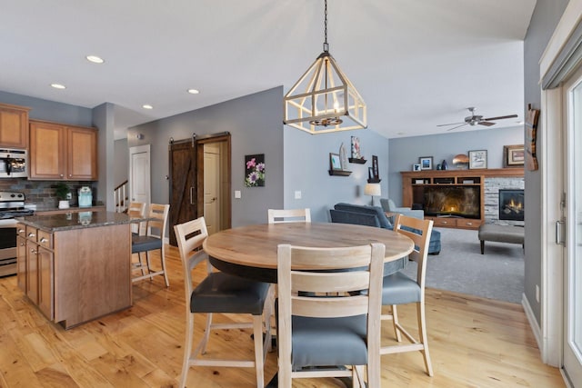 dining space with light hardwood / wood-style flooring, ceiling fan, a barn door, and a fireplace