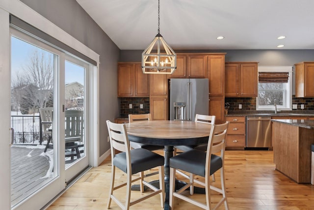 kitchen featuring light wood-type flooring, dark stone countertops, sink, appliances with stainless steel finishes, and pendant lighting