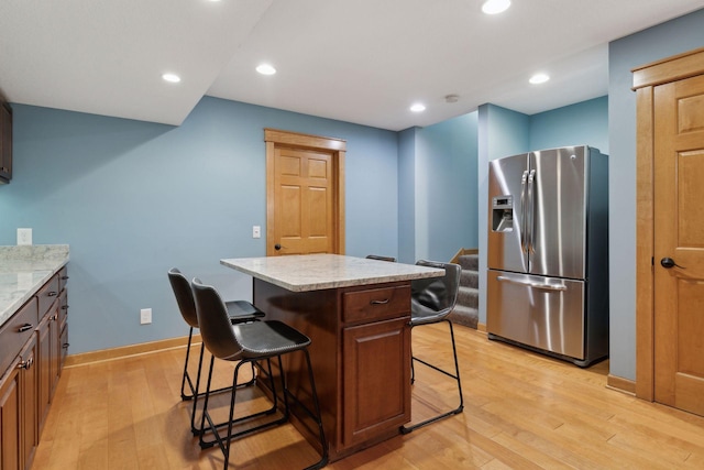 kitchen with a breakfast bar, stainless steel refrigerator with ice dispenser, light wood-type flooring, a kitchen island, and light stone countertops