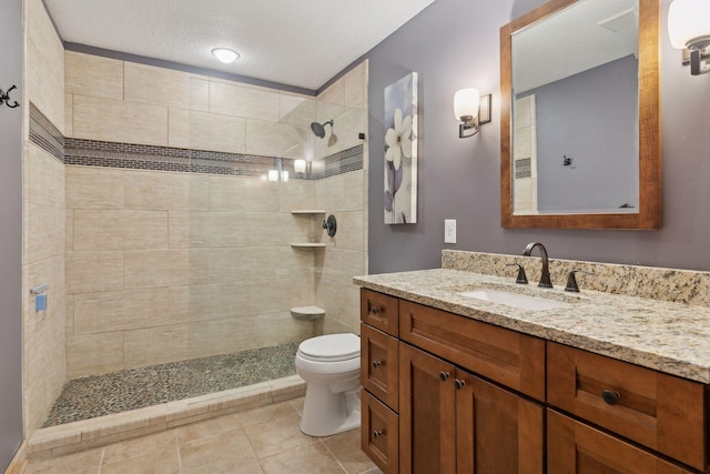 bathroom with vanity, a tile shower, a textured ceiling, toilet, and tile patterned floors