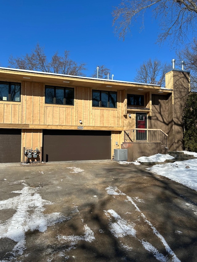 view of front of home with central air condition unit, a chimney, driveway, and an attached garage