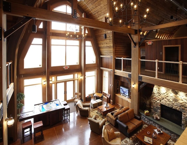 living room featuring wooden walls, high vaulted ceiling, an inviting chandelier, a stone fireplace, and wood ceiling