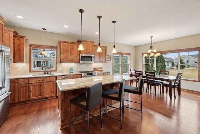 kitchen with dark wood-type flooring, a sink, stainless steel appliances, brown cabinetry, and decorative backsplash