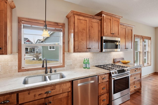 kitchen featuring a sink, light stone counters, hardwood / wood-style floors, stainless steel appliances, and decorative backsplash