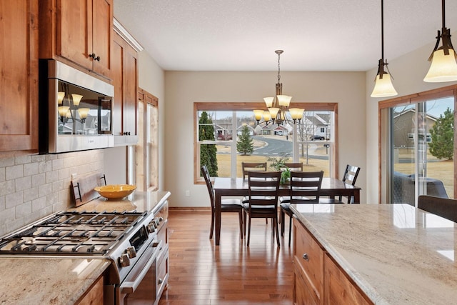 kitchen with light stone countertops, brown cabinets, hardwood / wood-style flooring, appliances with stainless steel finishes, and tasteful backsplash