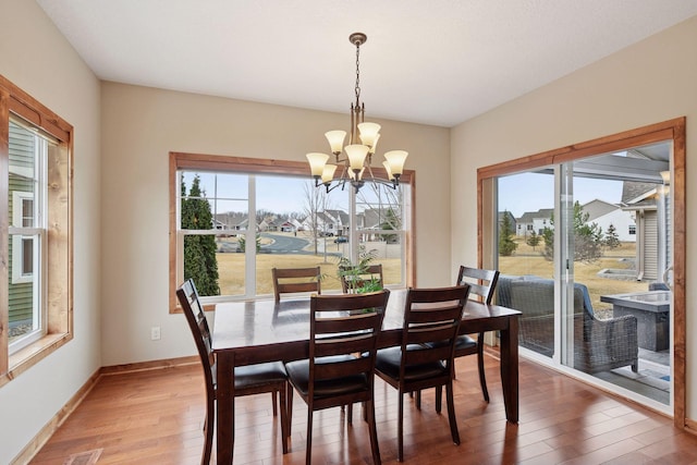 dining space featuring light wood-type flooring, baseboards, a notable chandelier, and a healthy amount of sunlight