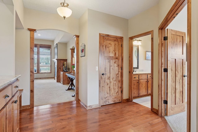 hallway featuring arched walkways, baseboards, light wood-style floors, and decorative columns