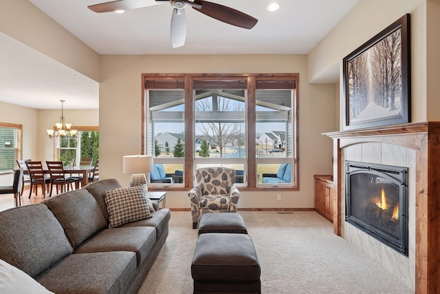 living room with a tiled fireplace, ceiling fan with notable chandelier, baseboards, and carpet