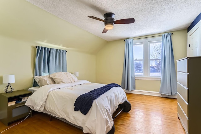 bedroom featuring light wood-type flooring, vaulted ceiling, ceiling fan, and a textured ceiling