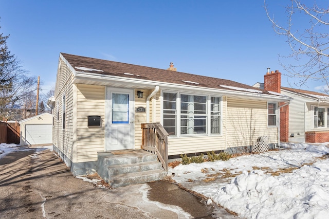 view of front of house featuring driveway, roof with shingles, a detached garage, and an outbuilding