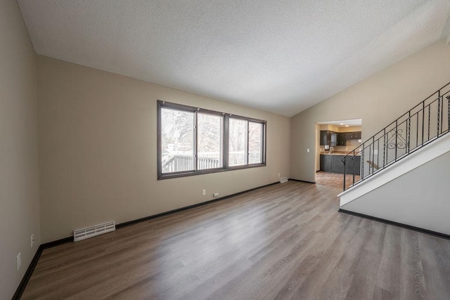 unfurnished living room with light wood-type flooring, lofted ceiling, and a textured ceiling