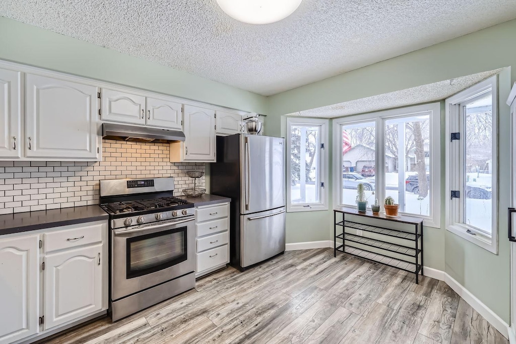 kitchen with tasteful backsplash, stainless steel appliances, a textured ceiling, white cabinets, and light wood-type flooring