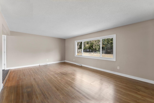 empty room featuring dark wood finished floors, visible vents, baseboards, and a textured ceiling