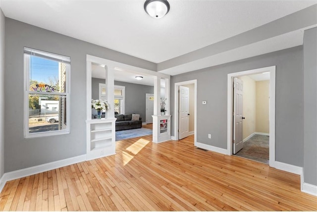 spare room featuring ornate columns, a healthy amount of sunlight, and light hardwood / wood-style flooring