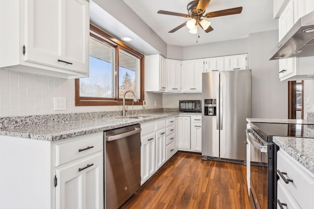 kitchen with appliances with stainless steel finishes, sink, white cabinetry, wall chimney range hood, and light stone countertops