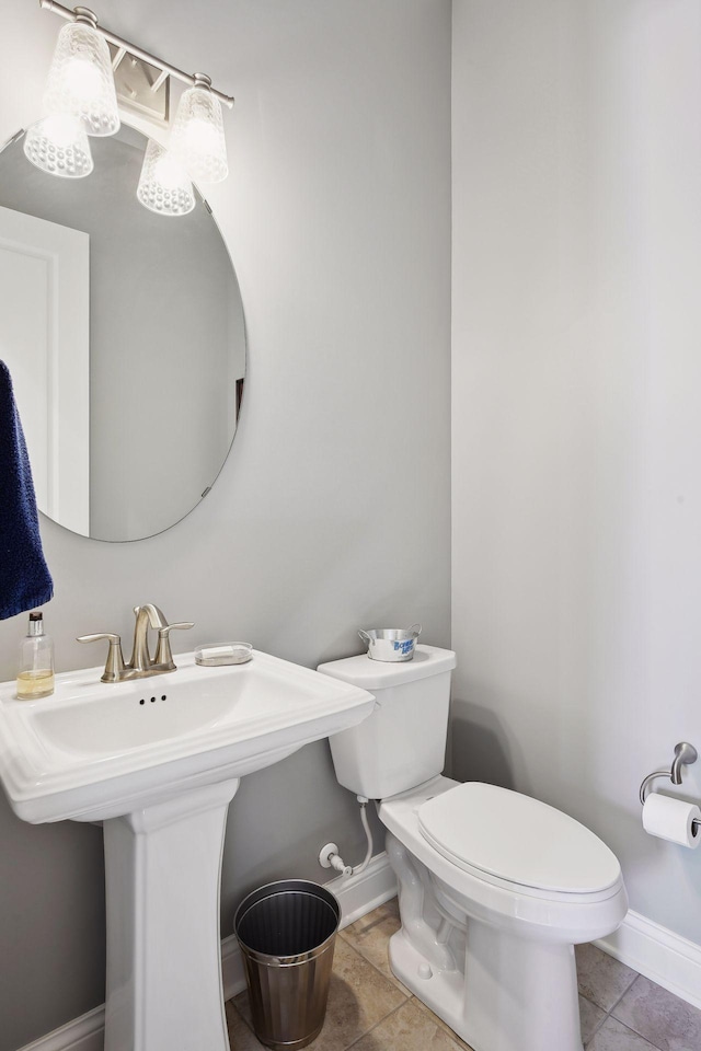 half bath with tile patterned floors, a sink, toilet, and baseboards