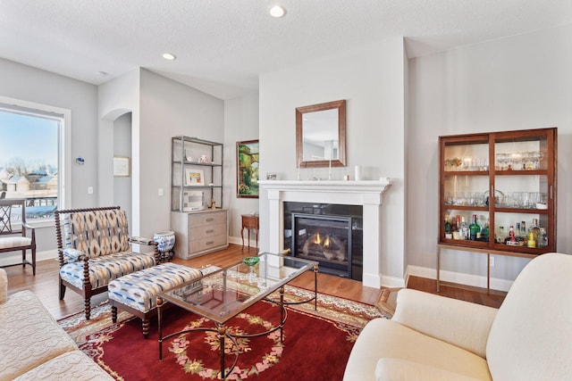 living area featuring a textured ceiling, wood finished floors, and a glass covered fireplace