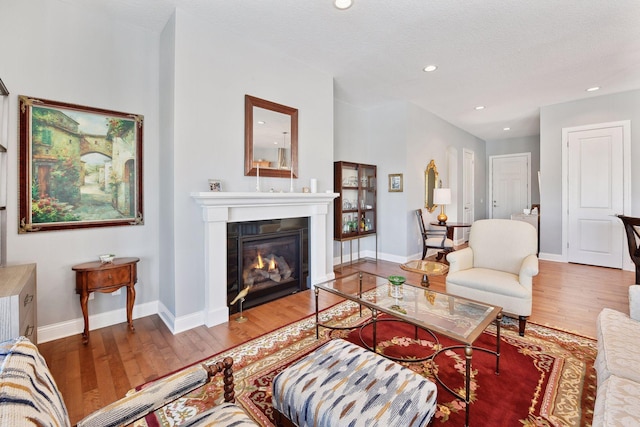 living area with a textured ceiling, recessed lighting, wood finished floors, baseboards, and a glass covered fireplace