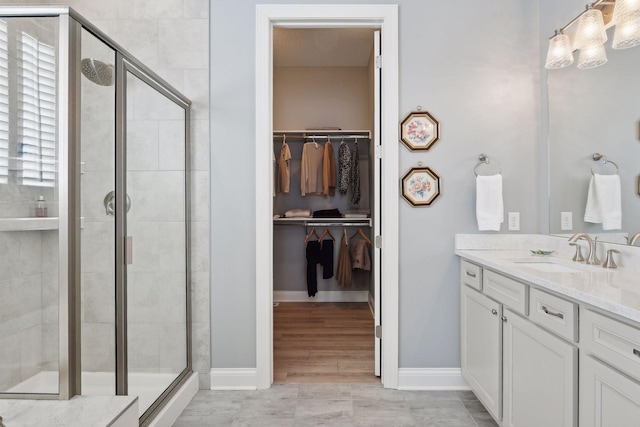 full bath featuring a shower stall, baseboards, a walk in closet, and vanity