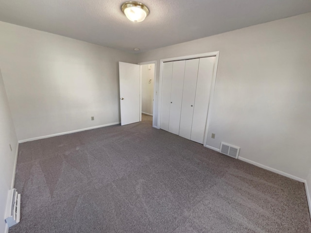 unfurnished bedroom with dark carpet, a closet, a textured ceiling, and baseboard heating