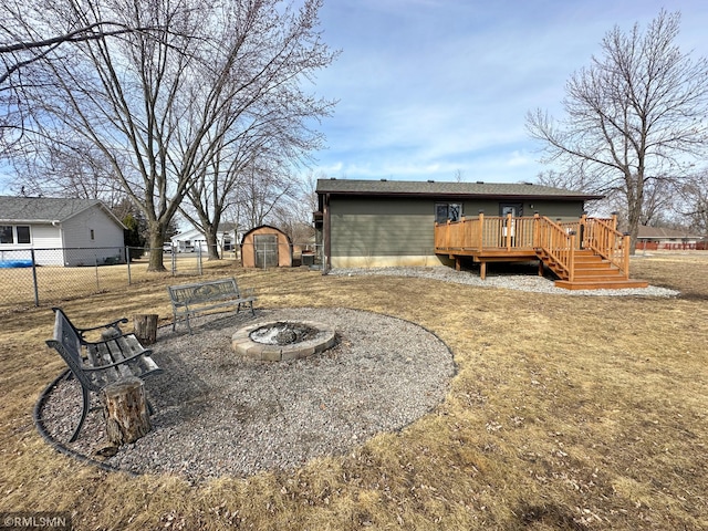 view of yard with a fire pit, fence, a deck, an outbuilding, and a storage unit